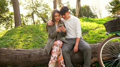 Young couple sharing a smartphone in a park Stock Footage 303484808