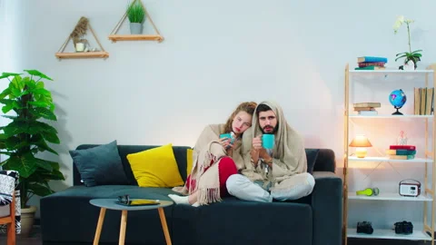 A young couple shivering on the couch and drinking something out of a blue mug Stock Footage 156402736