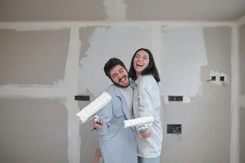 Young couple singing with paint rollers and laugh while painting walls. Stock Photos