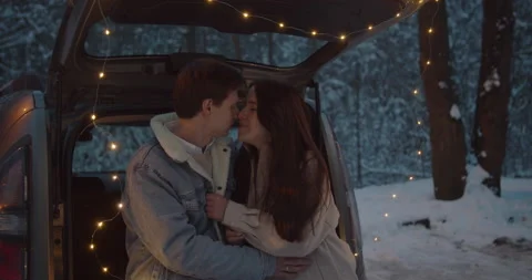 Young couple sit in a car trunk surrounded by christmas lights embracing Video stock 152467062