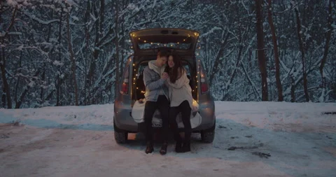 Young couple sit in a car trunk surrounded by christmas lights embracing Video stock 152467111