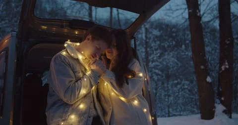 Young couple sit in a car trunk surrounded by christmas lights embracing Video stock 152467471