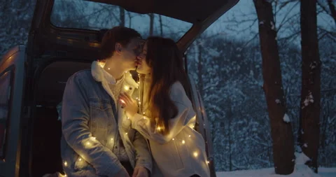 Young couple sit in a car trunk surrounded by christmas lights embracing Video stock 152467780