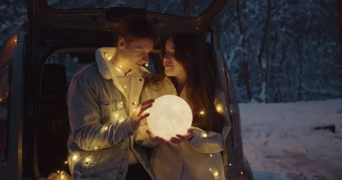 Young couple sit in a car trunk surrounded by christmas lights embracing Video stock 152468047