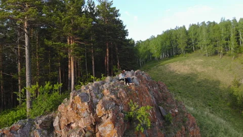 A young couple sit on the edge of a cliff and enjoy the beautiful view. Stock Footage 111120347