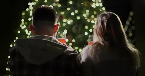 A young couple sits against the backdrop of a beautiful New Year tree, admiring Stock Footage 250999049