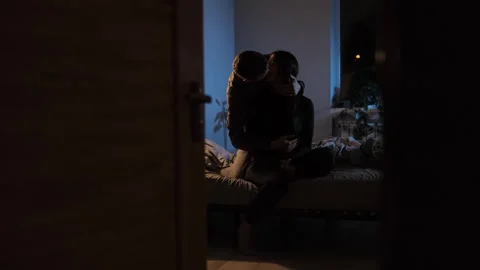 A young couple sits on a bed, hugging and kissing under warm evening lighting Stock Footage 300773065