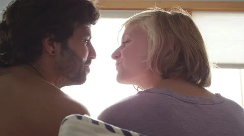 A young couple sits in bed together and kiss, as shot from behind Vídeo Stock 43671450