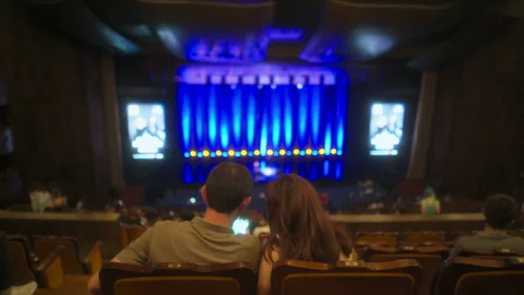 Young couple sits in chairs in half-empty concert hall before show starts Stock Footage 253061446