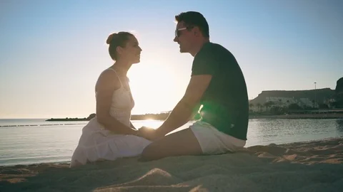 A young couple sits on the sandy seashore, smiles, kisses and holds each other's Stock Footage 104248175