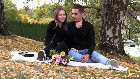 A young couple sits on a white bedspread in autumn park Stock Footage 96193157