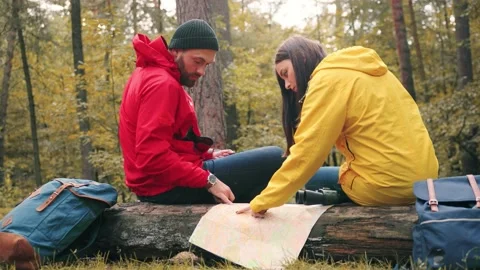 Young couple sits in woods on deck unfolding paper map and looking for the right Stock Footage 147072916