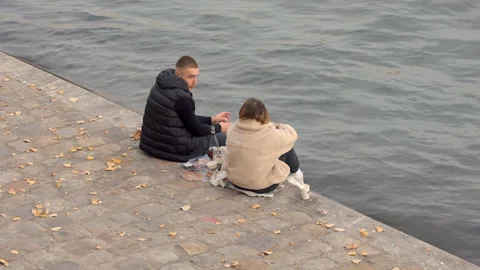 Young couple sitting and having a picnic on the bank of the Seine river in Paris Stock Footage 224140441