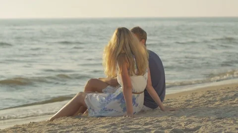 Young couple sitting and talking with each other at the beach on a peaceful day Stock Footage 73780106