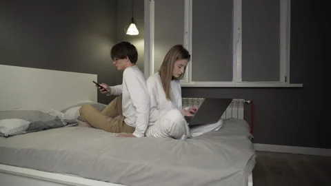 Young couple is sitting back to back on a bed in an apartment. Stock Footage 263471365