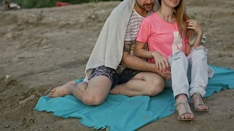 Young couple sitting on the beach hiding behind a blanket Stock Footage 79603608