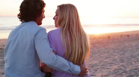 Young Couple Sitting on Beach at Sunset Stock Footage 21921682