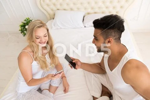 Young Couple Sitting In Bed, Happy Smile Hispanic Man And Woman Using Cell Smart