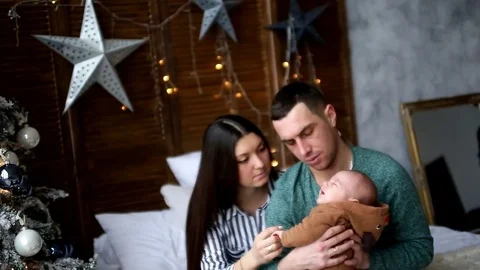 Young couple sitting on the bed holding the baby near the Christmas tree Stock Footage 85434097
