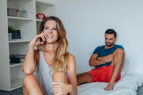 Young couple is sitting on the bed while woman is talking by the phone. Stock Photos
