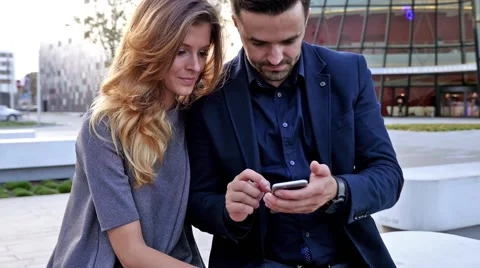 Young couple  sitting on a bench and using mobile phone. Positive emotions. Stock Footage 55390774