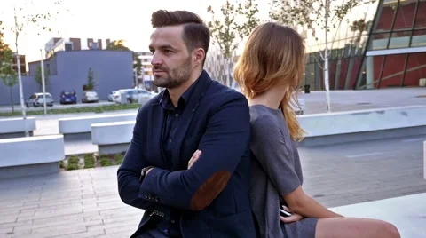 Young couple  sitting on a bench back to back. Outdoor photo. Stock Footage 55390883