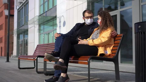 Young Couple Sitting on a Bench, Faces Covered with Protective Masks Stock Footage 132502733