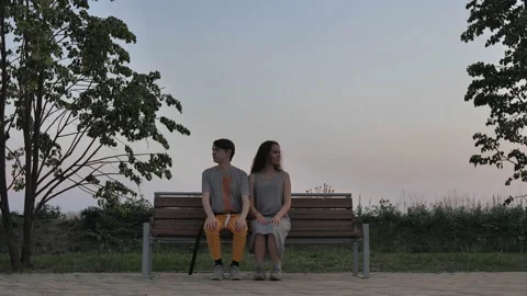 Young couple sitting on a bench facing the camera Stock Footage 135736255