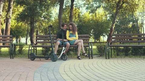 Young couple sitting on the bench in the park with electric scooters Stock Footage 137646146