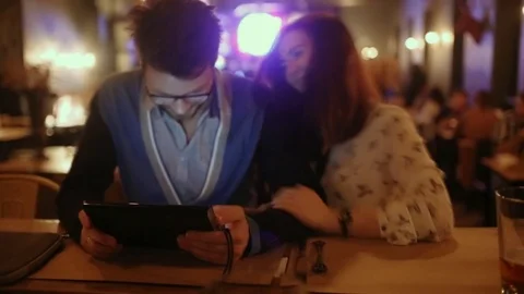 Young couple sitting in a cafe and look at the tablet Stock Footage 73424656