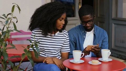 Young couple sitting in cafe and looking at smartphone. Two cups of coffee Stock Footage 81833341
