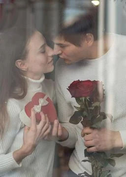 Young couple sitting in caffe window with bouquet of roses and heart gift box Stock Photos
