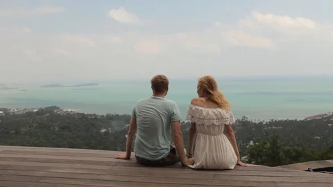 Young couple sitting on a cliff overlooking a tropical island Stock Footage 85935113