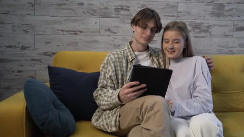 Young couple is sitting on the couch and video chatting on a tablet computer Stock Footage 259273632