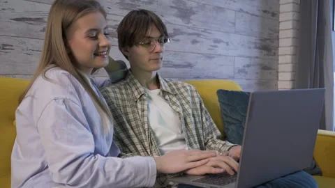 Young couple is sitting on the couch, looking at a laptop and talking Video stock 260228687
