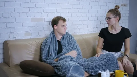 Young couple sitting on the couch. Sick, sad man sneezes, worried woman gives Stock-Footage 120037401
