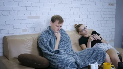 Young couple sitting on the couch. Sick, sad man sneezes, the woman complains Stock-Footage 120037420