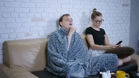 Young couple sitting on the couch. Sick man sneezing, a woman complains, pull Stock-Footage 120037439