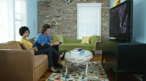 Young couple sitting on the couch watching television on a flat screen Stock Footage