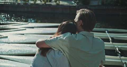 Young couple sitting on the dock hugging back view Stock Footage 221317799