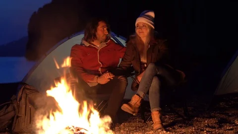Young couple sitting by the fire. camping with tents by the sea. spring evening. Stock Footage 107790420