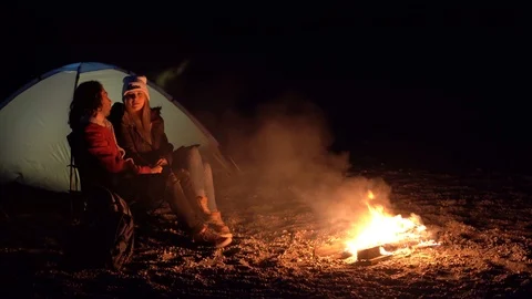 Young couple sitting by the fire. camping with tents by the sea. spring evening. Stock Footage 107797280