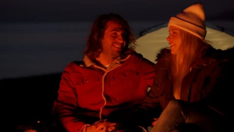 Young couple sitting by the fire. Camping with tents by the sea Stock Footage 107952028