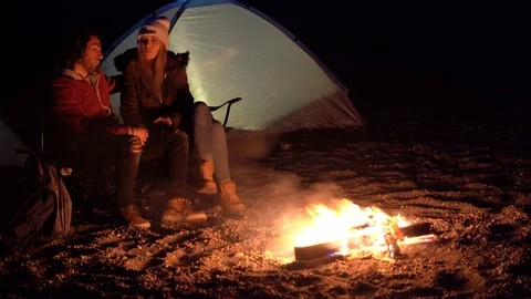 Young couple sitting by the fire. Camping with tents by the sea Stock Footage 107955541