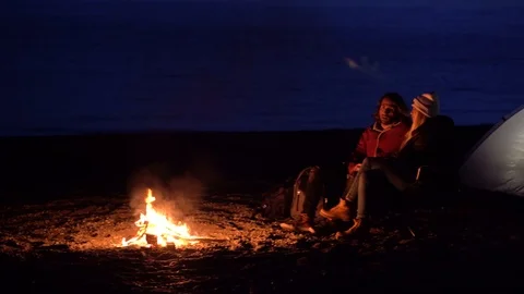 Young couple sitting by the fire. Camping with tents by the sea Stock Footage 107966474