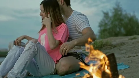 Young couple sitting by the fire on the coast Stock Footage 79603964