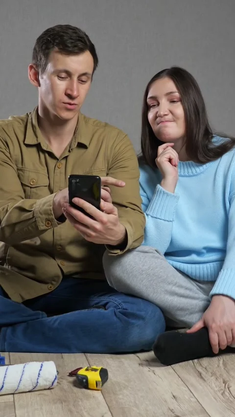 Young couple sitting on floor using smartphone to choose home renovation design Stock Footage 344799059