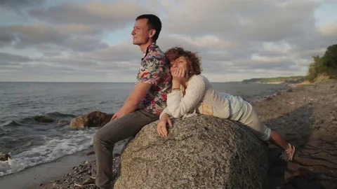 A young couple is sitting on a large rock by the sea. Video stock 78711772