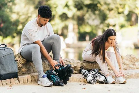 Young couple sitting on a park puting on inline skates Stock Photos