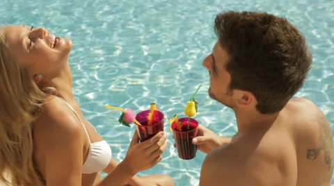 Young couple sitting by side of pool with drinks Video stock 43624277